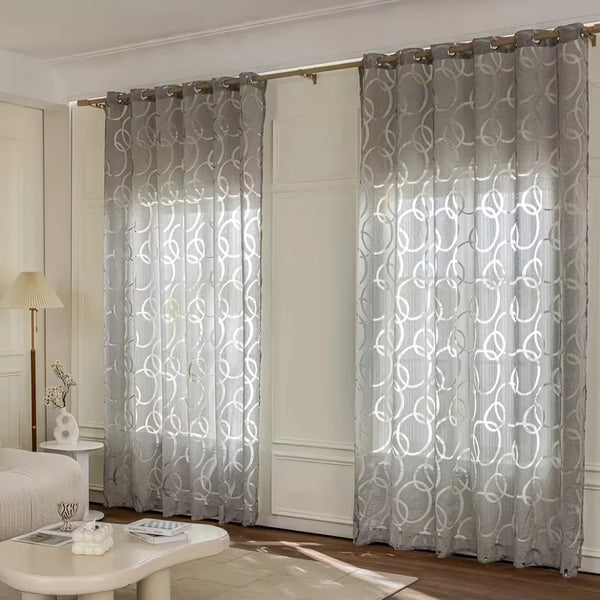 Modern geometric embroidered sheer curtain in gray covering a window.