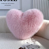 A fluffy pink heart-shaped throw pillow made of fox fur resting on a white sofa.