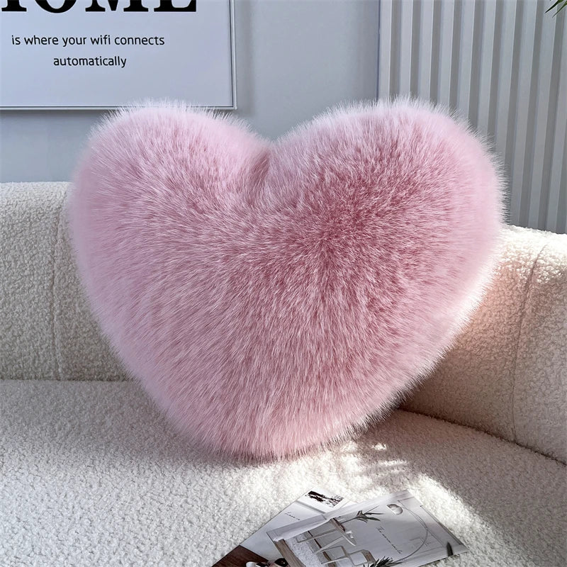 A fluffy pink heart-shaped throw pillow made of fox fur resting on a white sofa.