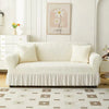 A cream-colored jacquard elastic sofa cover with a gathered skirt displayed in a bright, modern living room.