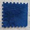 A deep blue plush interlocking puzzle rug mat placed on a light-colored surface.