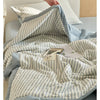 A light blue and white striped luxury jacquard summer quilt draped over a bed.