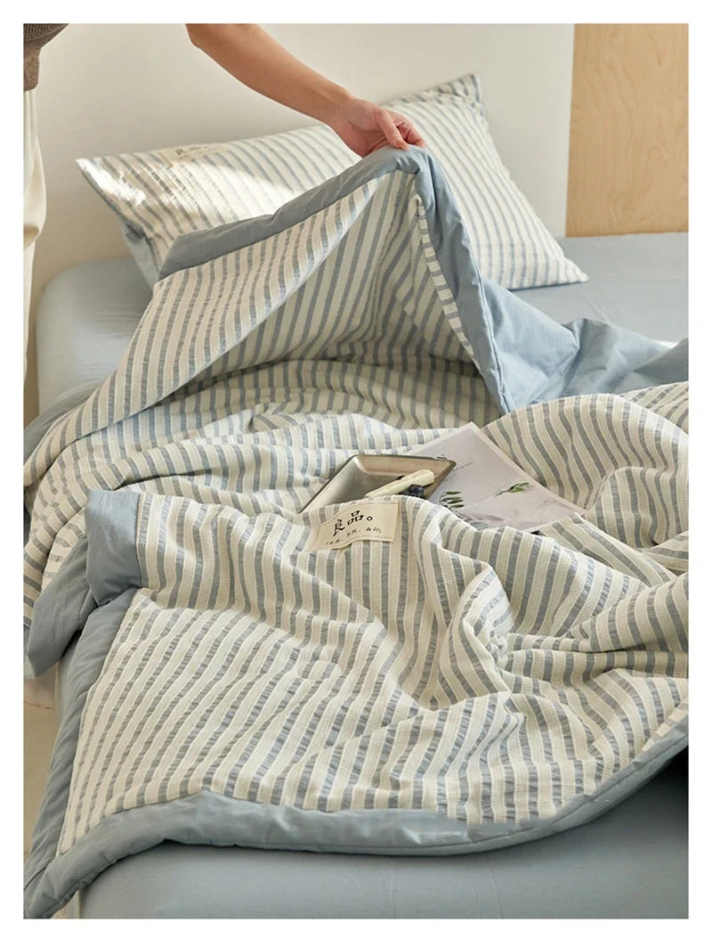 A light blue and white striped luxury jacquard summer quilt draped over a bed.