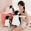 A young woman is sitting on a couch with several black and white penguin plush toys.