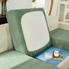 A close-up of a sage green jacquard sofa slipcover with a white cushion and elastic edges.