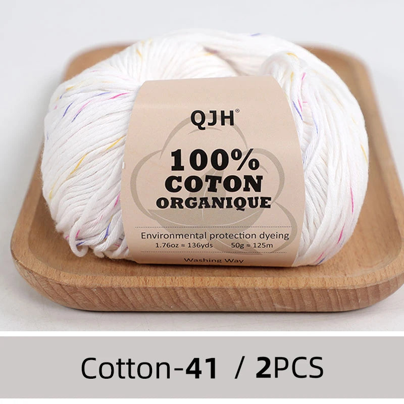A ball of white organic cotton yarn labeled QJH 100% COTON ORGANIQUE resting on a wooden board.