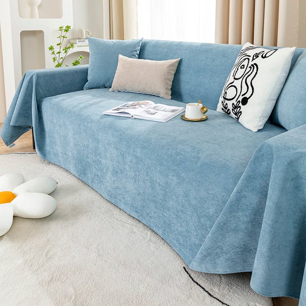 A light blue waterproof sofa cover blanket draped over a sofa with pillows and an open book.