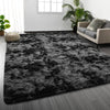 A dark gray shaggy rug with a fluffy texture placed on a wooden floor in a bright room.