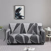 A gray elastic sofa cover protector featuring a geometric pattern and a framed tropical leaf print artwork on the wall.
