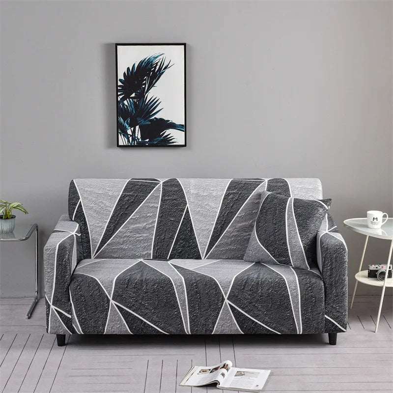 A gray elastic sofa cover protector featuring a geometric pattern and a framed tropical leaf print artwork on the wall.