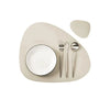 A set of beige reusable vinyl placemats, a white plate, and silverware are displayed on a light background.