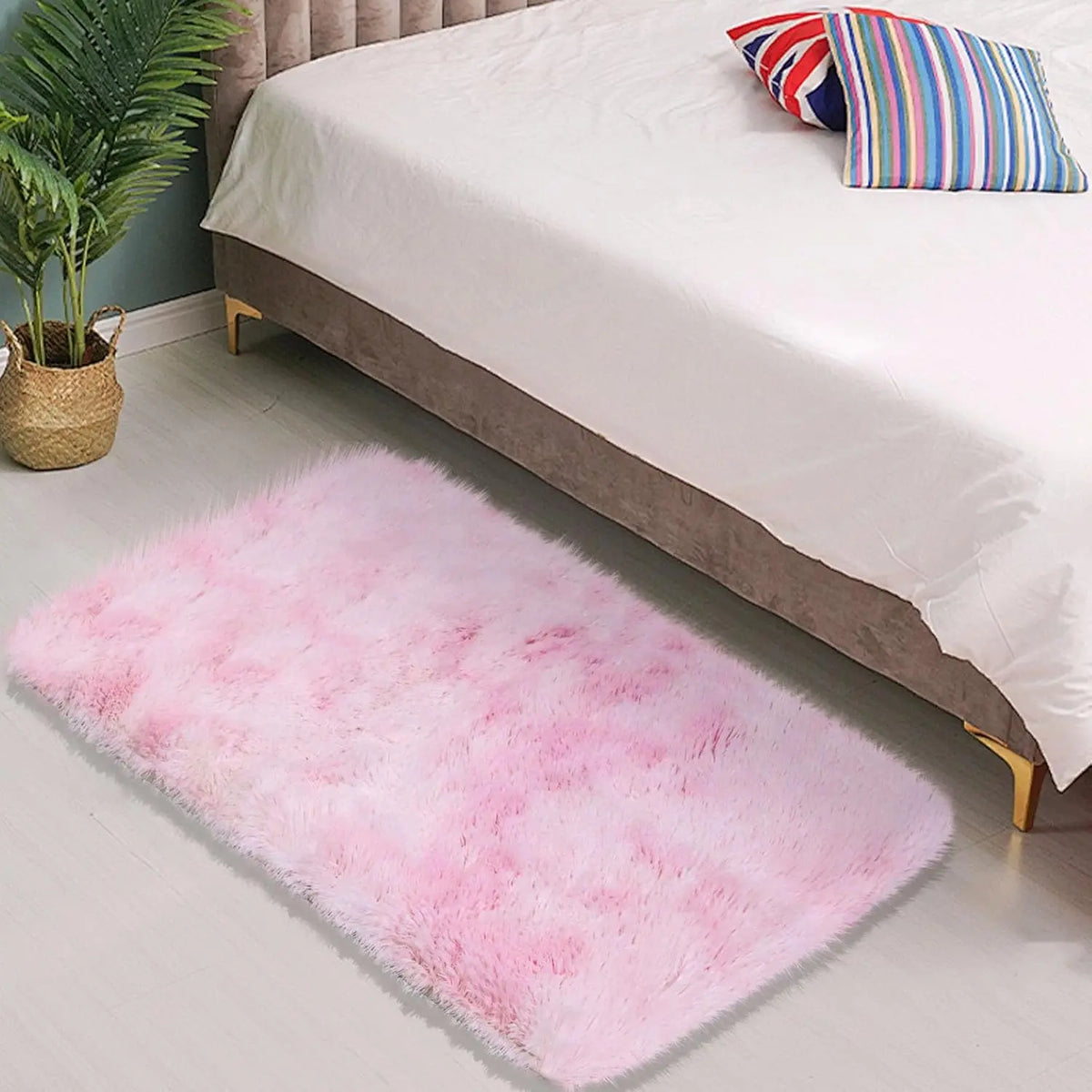 A fluffy pink area rug placed on a light wooden floor next to a bed with white linens.