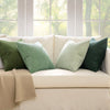 A set of four textured throw pillow covers in shades of olive green and sage green on a cream sofa.