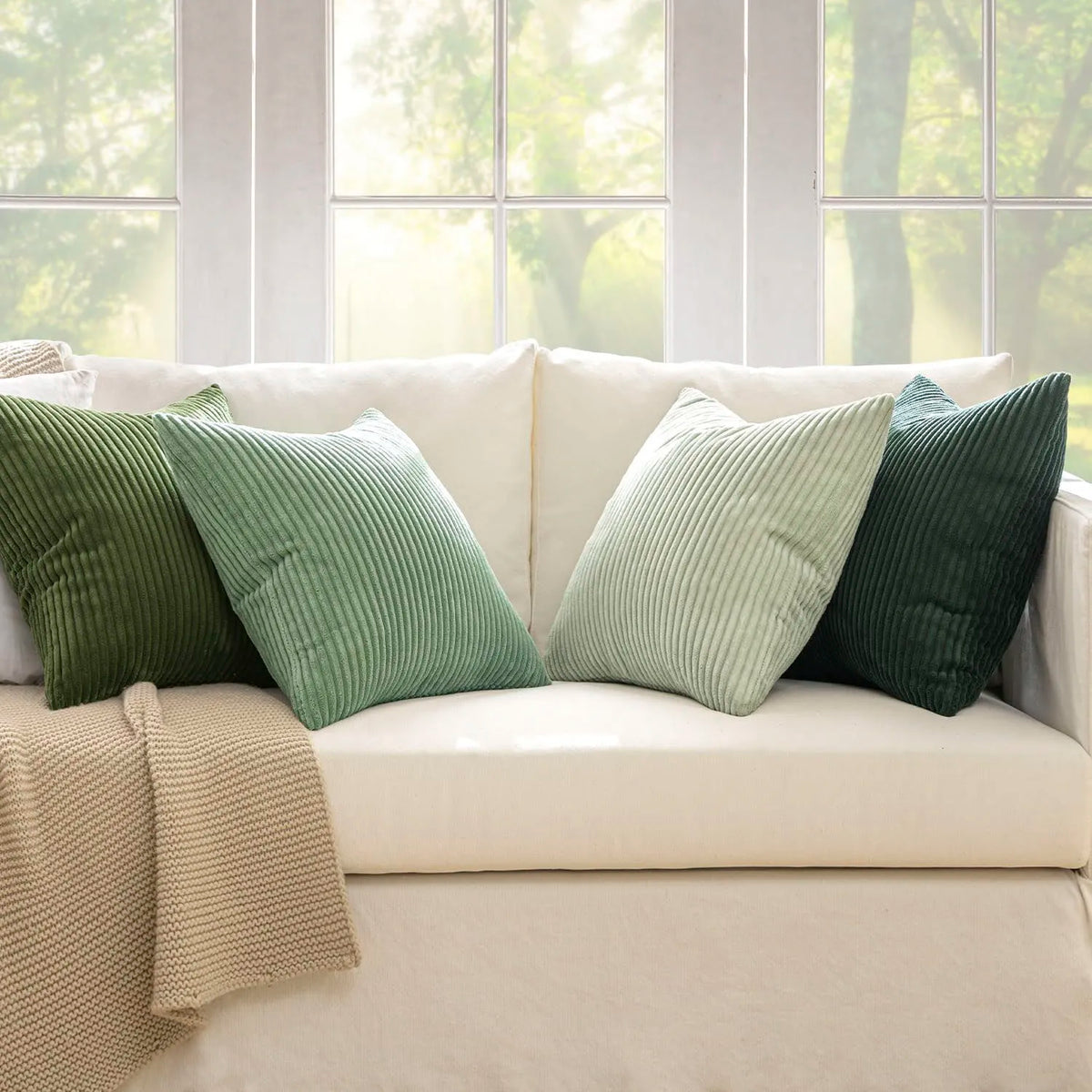 A set of four textured throw pillow covers in shades of olive green and sage green on a cream sofa.