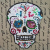 A white sequin skull embroidered clothing patch with colorful accents on a beige fabric background.