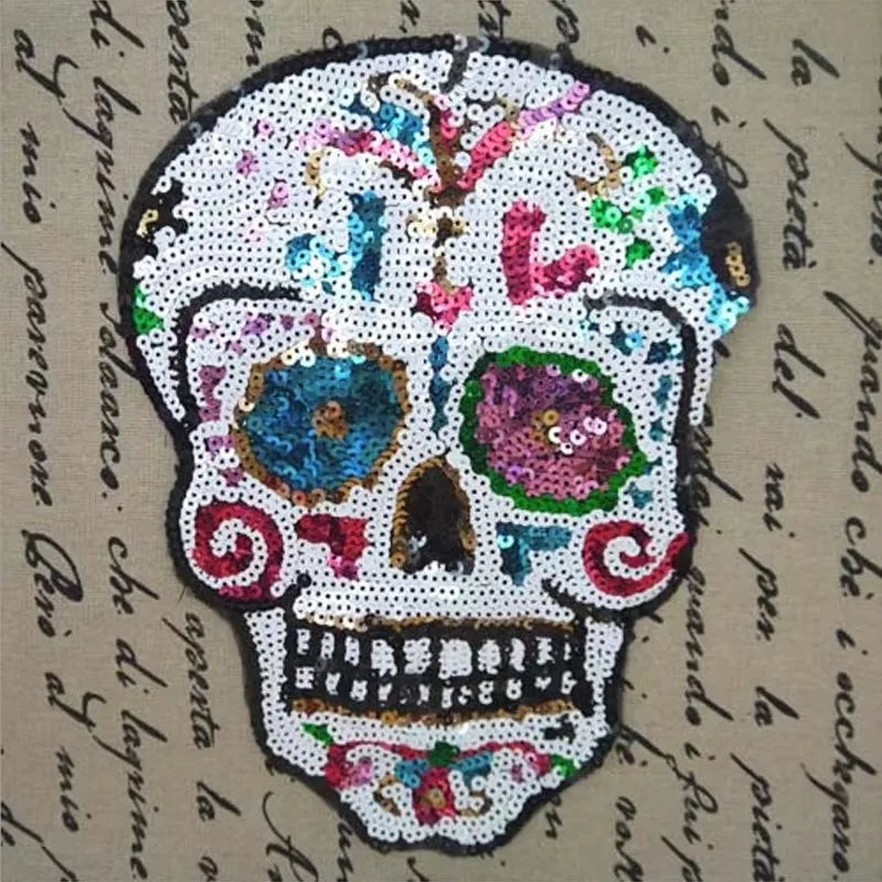 A white sequin skull embroidered clothing patch with colorful accents on a beige fabric background.