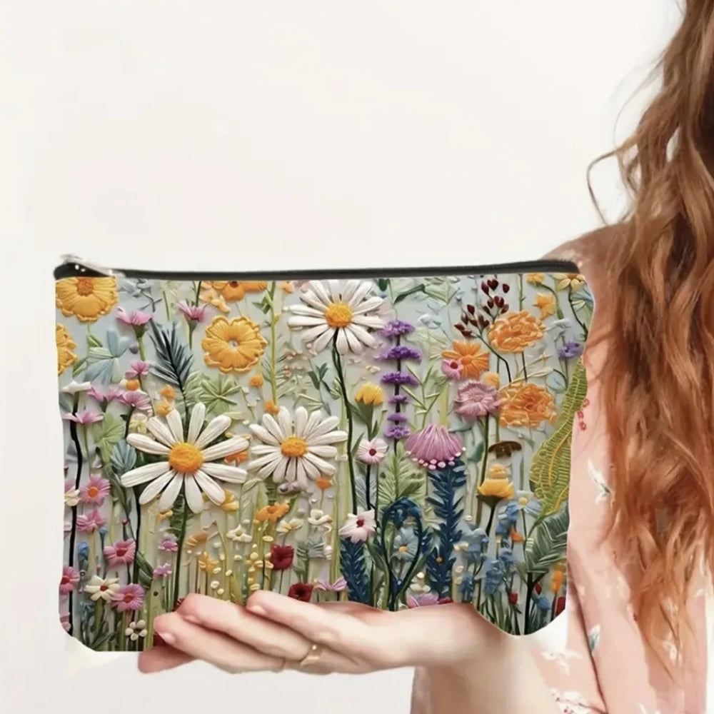 A hand holds a floral double-sided cosmetic storage pouch featuring various dried flowers and greenery.