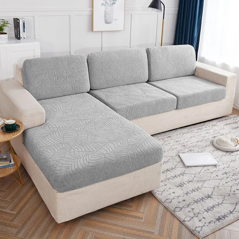 A light gray waterproof jacquard stretch sofa cover displayed on a beige sofa in a bright room.