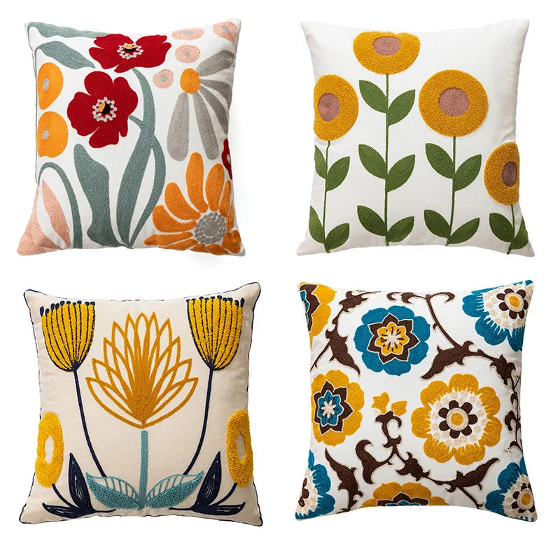 Four throw pillows featuring embroidered floral designs in shades of red, orange, yellow, and green on a white background