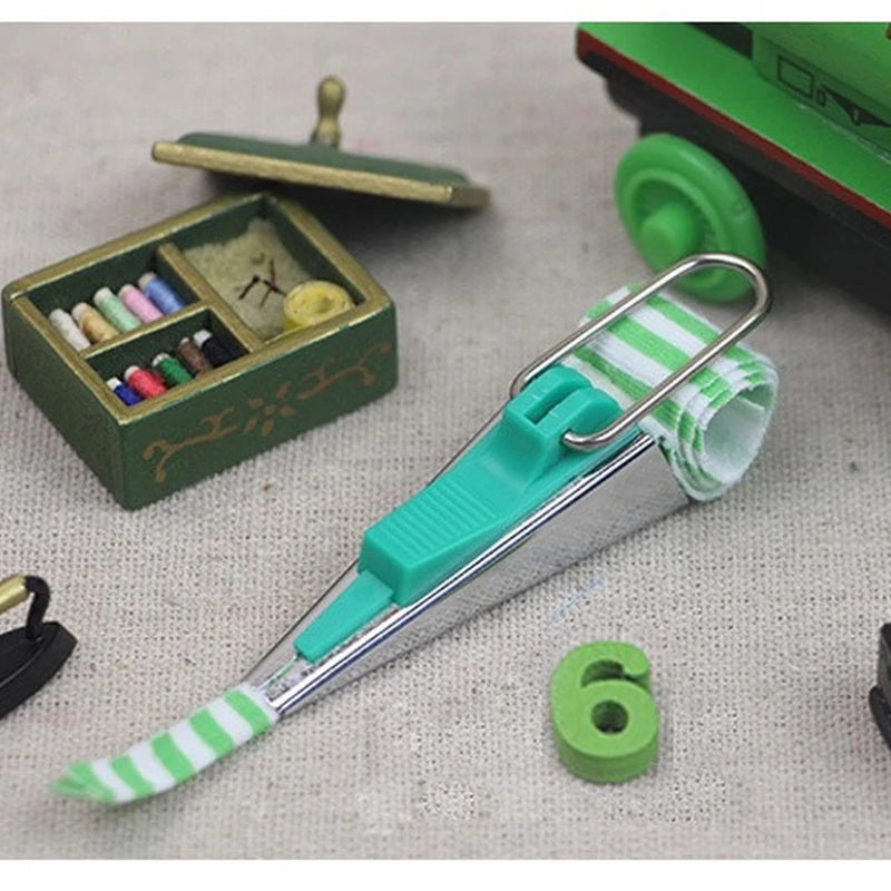 A precision bias tape maker tool in light blue and silver with a green and white striped tape visible.