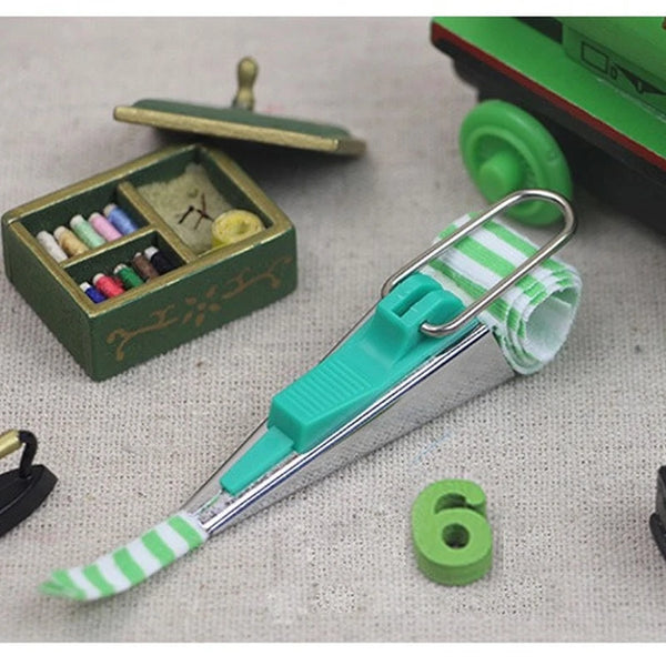 A precision bias tape maker tool in light blue and silver with a green and white striped tape visible.