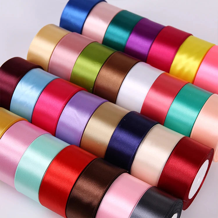 A collection of rolled satin ribbon in various colors including pink, green, purple, and red for crafts and gift wrapping.