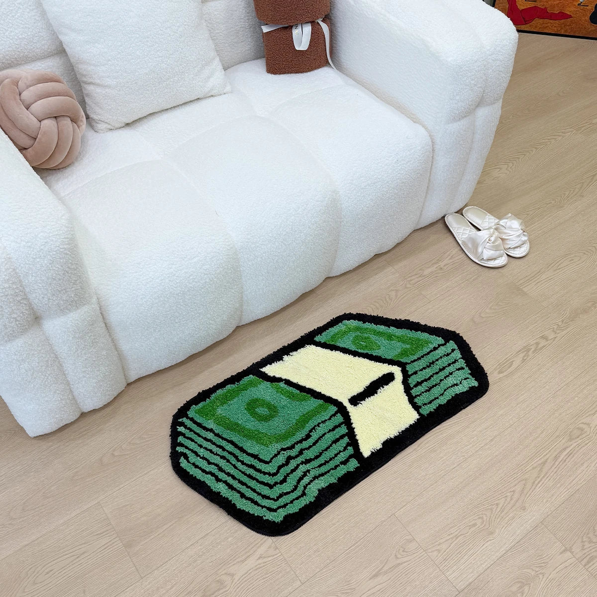 A green and yellow tufted rug shaped like a dollar bill lying on a light wood floor next to a white sofa.