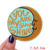 An embroidered iron-on patch featuring the text You Are My Sun Shine on a light blue background with an orange border.
