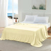 A light yellow ice silk cooling blanket is draped over a bed in a bright bedroom setting.