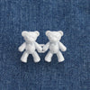 A pair of white bear button pins are displayed on a blue denim fabric.
