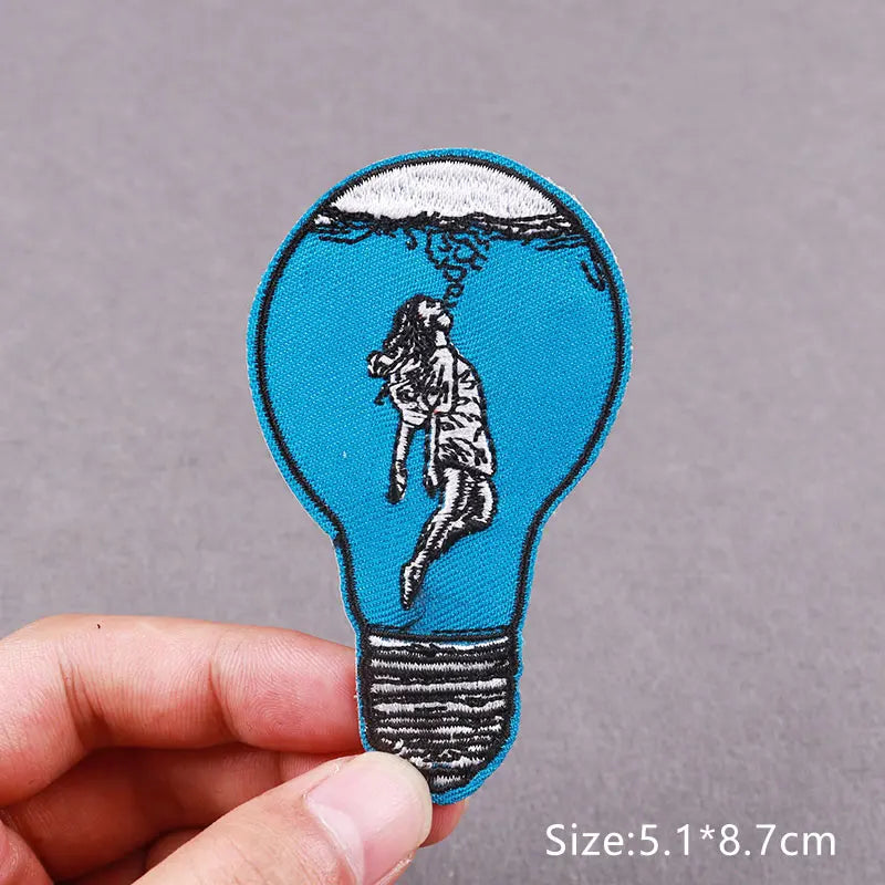 An embroidered patch shaped like a lightbulb containing a figure, possibly a horror movie character.