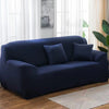 A dark navy stretch sofa cover with throw pillows placed in a bright living room setting.