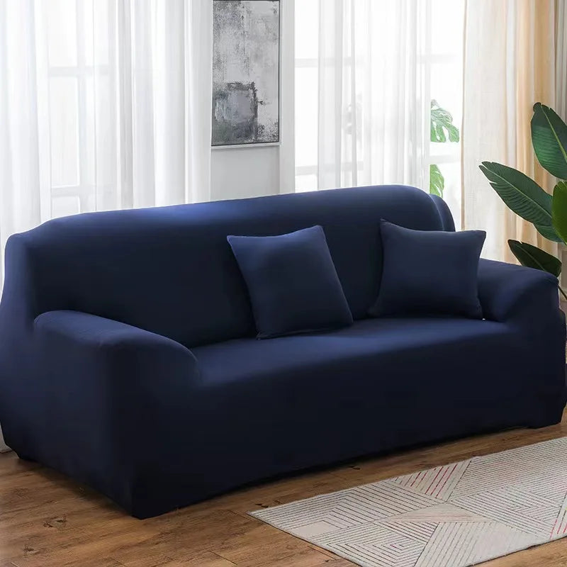 A dark navy stretch sofa cover with throw pillows placed in a bright living room setting.