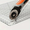 A precision acrylic quilting ruler with an orange and gray handle is shown resting on a clear grid surface.