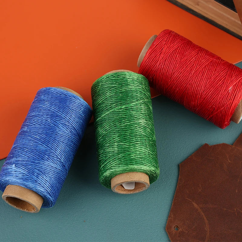 Three spools of waxed thread in red, green, and blue next to a brown leather tag.