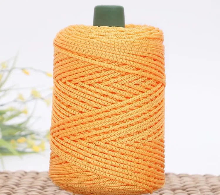 A spool of bright orange crochet ice rope with a dark green cap, lying on a woven surface.