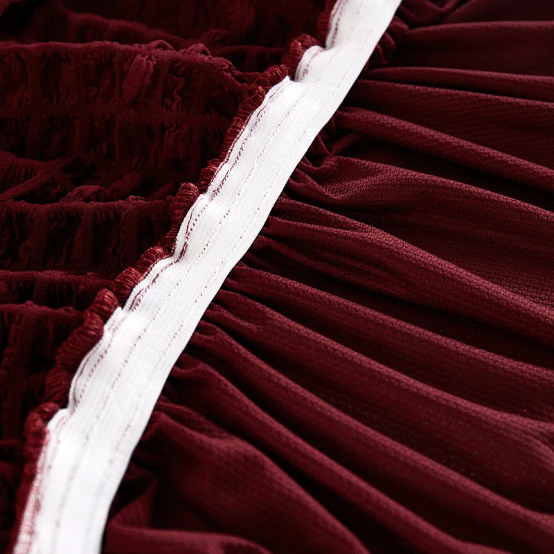 A close-up of a deep burgundy stretch knit sofa cover with white piping and bubble lattice texture.