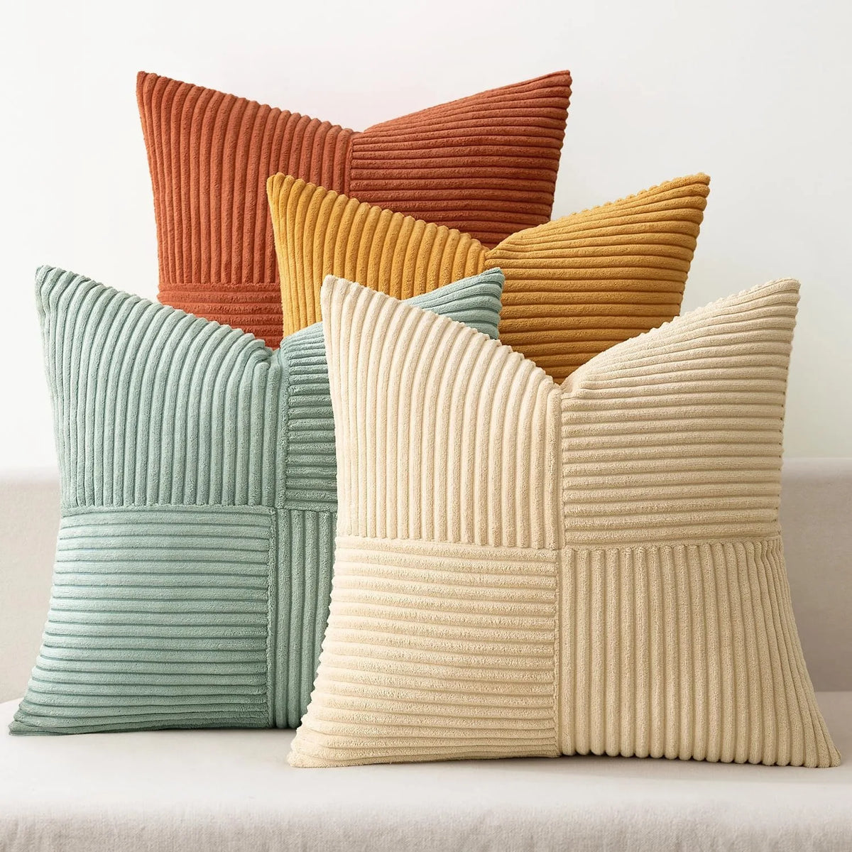 A set of four neutral corduroy throw pillow covers in shades of orange, yellow, and beige with a patchwork design.