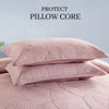 Two pink embroidered cotton quilted pillow covers stacked on a pink quilted bed.