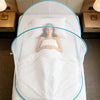 A white bed with a mosquito net draped over it, featuring a woman lying in the center.