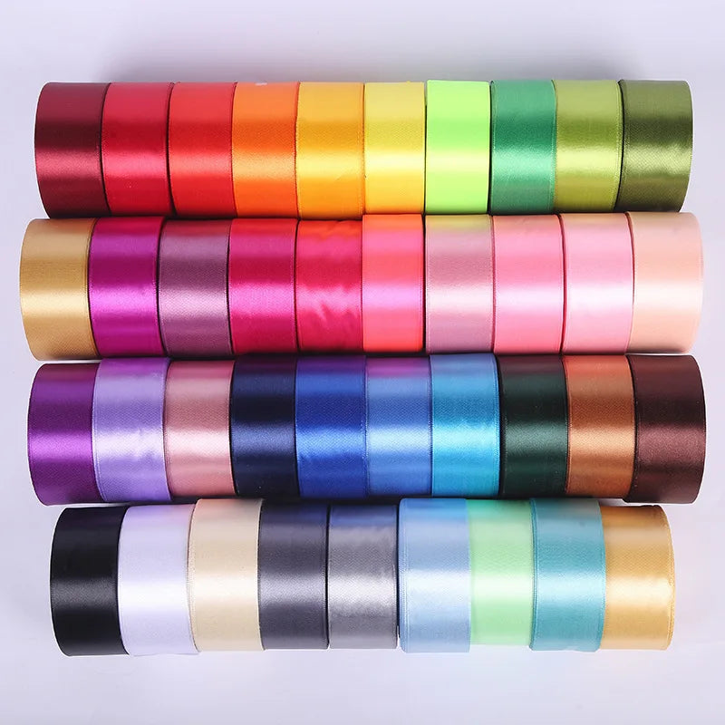 A collection of rolled satin craft ribbons in various shades including red, orange, yellow, green, pink, purple, blue, and br