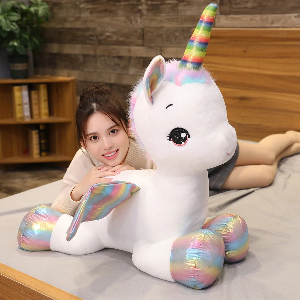 A white unicorn plush toy with a rainbow horn is lying down on a person's lap.