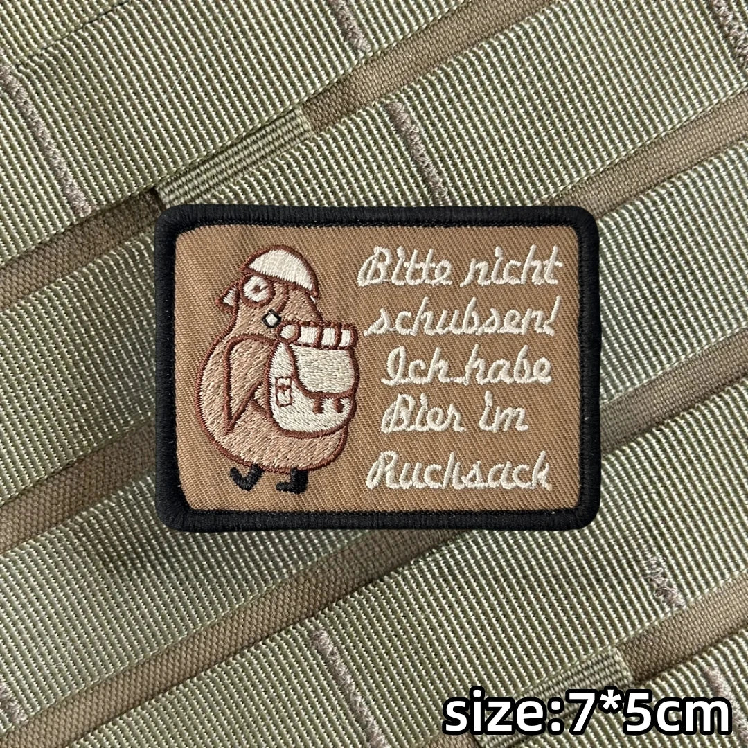 A square embroidered patch with text in German instructing not to push and stating that the item is in the back pocket.