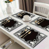 A set of black placemats featuring a vintage skull and floral mystic cross design on a white table.