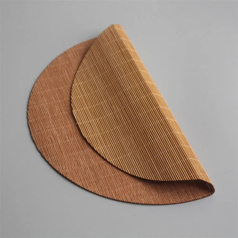 A curved, hand-woven bamboo tea mat in a natural brown color shown from a side angle.