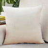 A square, cream-colored velvet cushion cover resting on a light-colored sofa.