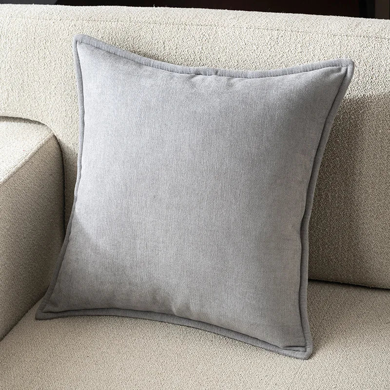 A square, light gray chenille throw pillow resting on a beige sofa cushion.