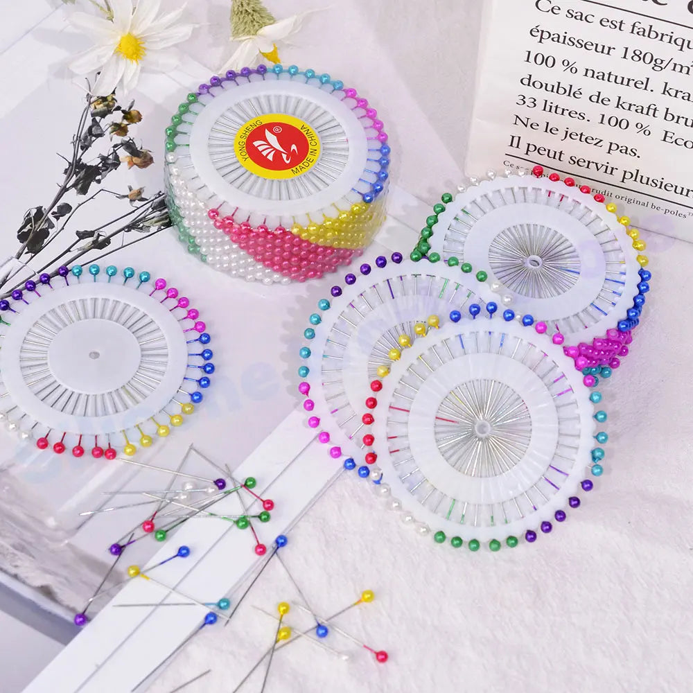 A collection of colorful pearl head pins for sewing and crafting displayed on a white surface.