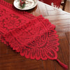 A red retro lace table runner with tassels laid on a wooden table next to a small plate.