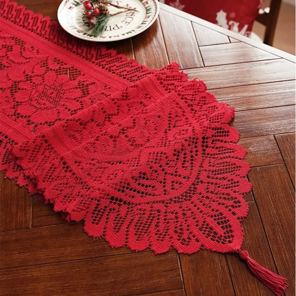 A red retro lace table runner with tassels laid on a wooden table next to a small plate.
